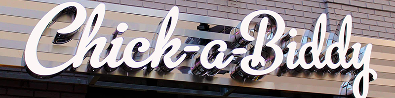 Illuminated channel letters above restaurant entrance, reading "Chick-A-Biddy" 